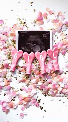 pink baby booties laying on top of confetti with the word ohh spelled out