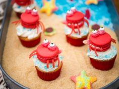 cupcakes decorated with red crabs and white frosting in a metal pan on a table