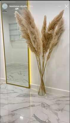 some dried flowers in a vase on a marble floor with a mirrored wall behind it