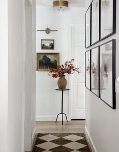 a hallway with pictures on the wall and a vase full of flowers in front of it