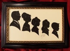 silhouettes of people in formal dress are framed in a black frame on a red cloth