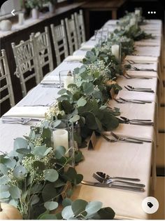 the long table is set with silverware and greenery