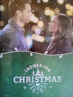 a man and woman standing next to each other in front of a christmas sign with snowflakes on it