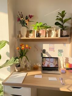 a laptop computer sitting on top of a wooden desk next to potted plants and flowers