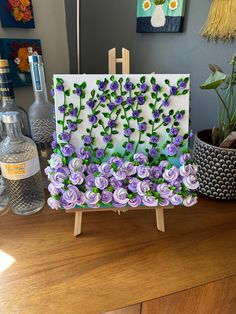 an easel with purple flowers on it sitting on a table next to a painting