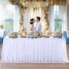 a bride and groom kissing in front of a table with flowers, candles and decorations