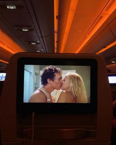 a couple kissing in front of a television screen on an airplane with orange lights above them