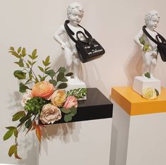 two small statues sitting on top of a black table next to flowers and vases