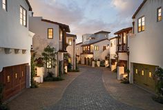 a cobblestone street lined with tall white buildings at dusk in an upscale neighborhood