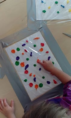 a young child is painting on a piece of paper with colored confetti sprinkles