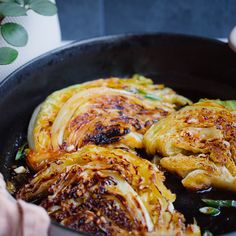 someone cooking cabbage in a skillet on the stove top with other food items nearby