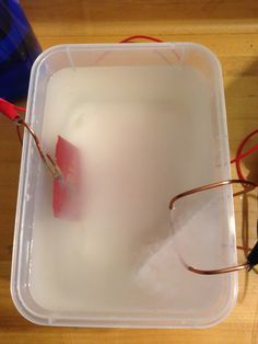 a plastic container filled with liquid and some wires attached to the lid on a wooden table