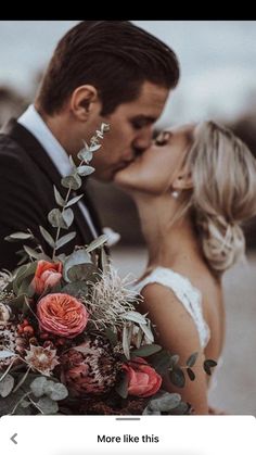 a bride and groom kissing each other in front of the camera with flowers on their bouquet