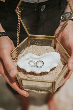 two wedding rings in a glass box with sand and sea salt inside it, held by hands