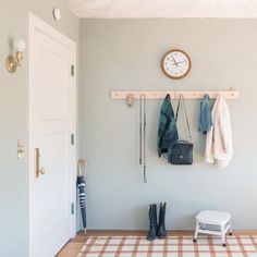 there is a clock on the wall next to some coats and boots hanging from hooks