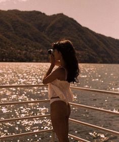 a woman standing on the deck of a boat looking at the water while holding a cell phone to her ear