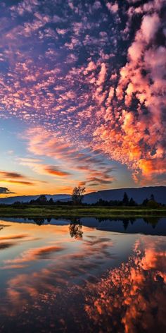 the sky is reflected in the still water at sunset with clouds and trees on the other side