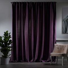 a chair sitting in front of a window covered in purple curtaining next to a potted plant