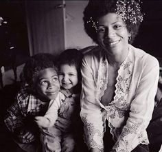 an older woman and two young children sitting on a bed smiling at the camera with their arms around each other