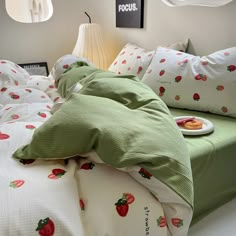 an unmade bed with green sheets and strawberry print on the comforter is shown