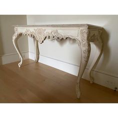 an antique white console table in the corner of a room with hard wood flooring