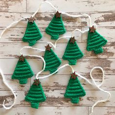 crocheted christmas tree ornaments hanging from string on wooden background with white yarn and twine