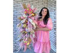 a woman holding a pink and gold christmas ornament in front of a brick wall