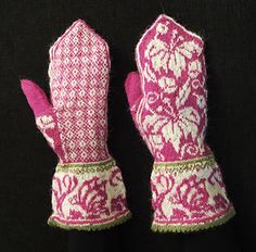 two pink and white mittens sitting on top of a black cloth covered table next to each other