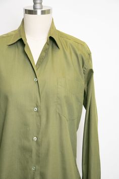 "Vintage 1950s ladies button down blouse in soft moss green cotton blend. Pointed collar. Relaxed yet feminine fit. Simple button front. Long sleeves that need cufflinks, not included. Unlined. Label: Adelaar man tailored shirt - Cotton + Darcon Fits like size: Medium Measurements: Bust: 38\" - 40\" pit tp pit Waist: 36\" Length: 22.5\" Shoulder to shoulder: 16\" Sleeve: 24\" Condition: Very good/good. Very minor under arm fade and a few faint marks that look oil based which didn't lift with soa Classic Single Breasted Collared Blouse, Collared Olive Shirt With Button Closure, Olive Collared Shirt With Button Closure, Classic Green Tops With Spread Collar, Classic Single Breasted Tops For Daywear, Classic Single-breasted Tops For Daywear, Classic Collared Blouse, Classic Collared Plain Blouse, Classic Green Shirt For Work