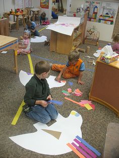 children are sitting on the floor making paper shapes