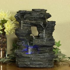 a water fountain sitting on top of a wooden table next to a vase with flowers