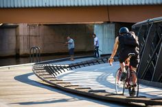 a man riding a bike across a bridge next to another person on a skateboard