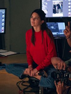 a woman sitting on the floor in front of two monitors and holding a video camera