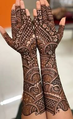 two hands with henna tattoos on their palms and arms, both decorated with intricate designs