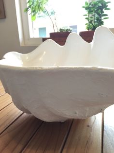 a white bowl sitting on top of a wooden table next to a potted plant