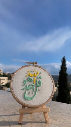 the embroidery is being displayed on an easel with a blue sky in the background