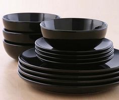 a stack of black plates sitting on top of a wooden table next to each other