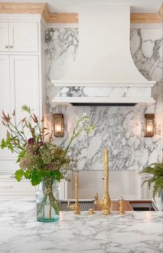 a kitchen with marble counter tops and gold faucets on the stove top, surrounded by white cabinets