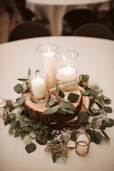 candles and greenery sit on top of a wood slice at a table with white linens