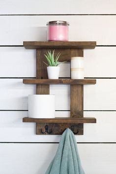 a bathroom shelf with two shelves holding candles, a towel and a potted plant