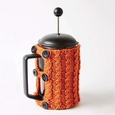 an orange knitted coffee pot cozy with black handles and button holes on the lid