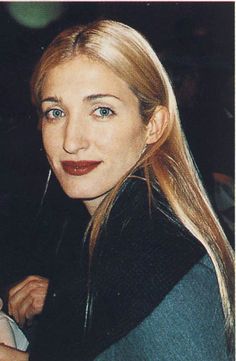 a woman with long blonde hair and blue eyes posing for a photo in a black jacket