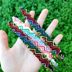 a hand holding three different colored bracelets in it's palm, with grass in the background