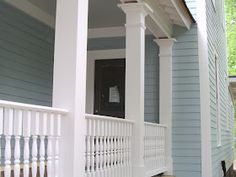 the front porch of a blue house with white pillars and railings on both sides