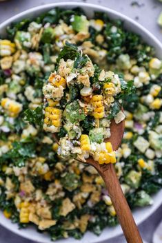 a wooden spoon filled with corn salad on top of a white plate next to other food