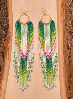 a pair of earrings with green, pink and white beaded fringes on wood