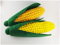 two stuffed corn cobs sitting side by side on a white surface, one is yellow and the other is green