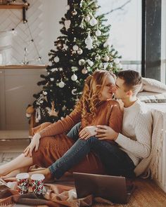 a man and woman sitting on the floor next to a christmas tree with presents under it