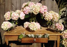 a wooden table topped with lots of pink and white hydrangeas on top of it