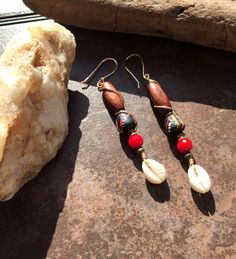 These 3 inch long dangles have gold toned wire wrappings around colorful Krobo beads. The Krobo beads are hand made by the Ashanti people in Ghana Africa.  The red multi faceted stones brighten up the wood and lightweight  cowrie shells that dangle from the bottom. The ear wires are handcrafted. The are one of a kind. Bohemian Adjustable Cowrie Shell Earrings, Hippie Dangle Earrings For Beach, Bohemian Cowrie Shell Earrings, Bohemian Cowrie Shell Earrings As Gift, Bohemian Cowrie Shell Earrings For Gift, Bohemian Earrings With Ear Wire For Vacation, Bohemian Teardrop Earrings For Vacation, Bohemian Brown Wire Wrapped Beaded Earrings, Bohemian Cowrie Shell Dangle Jewelry